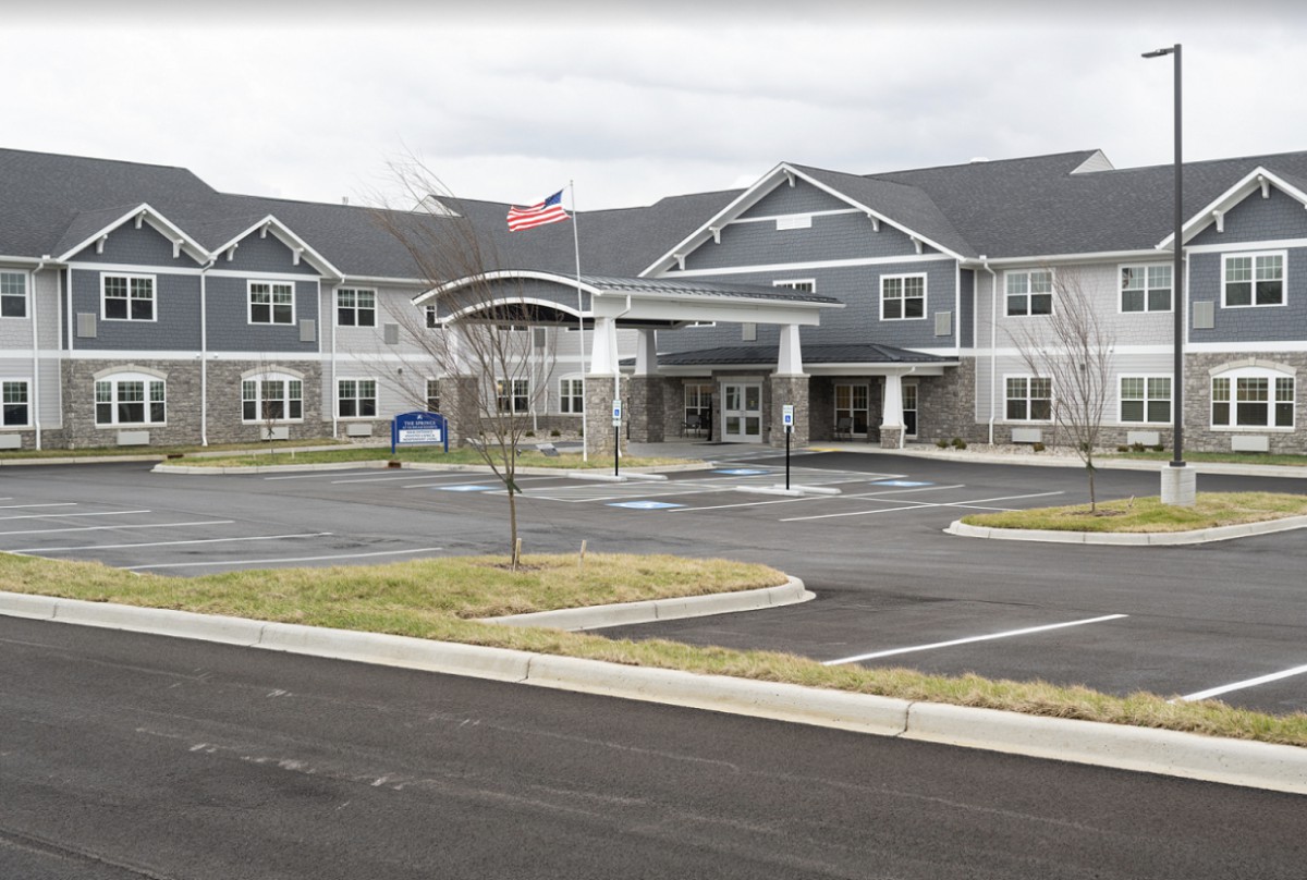 A large building with a parking area and an American flag in front, set against an overcast sky.
