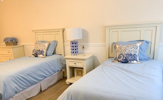 A cozy bedroom with two twin beds, featuring blue bedding and a decorative lamp on a nightstand.