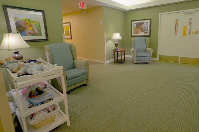 A cozy waiting room with green walls, comfortable chairs, and a magazine rack.