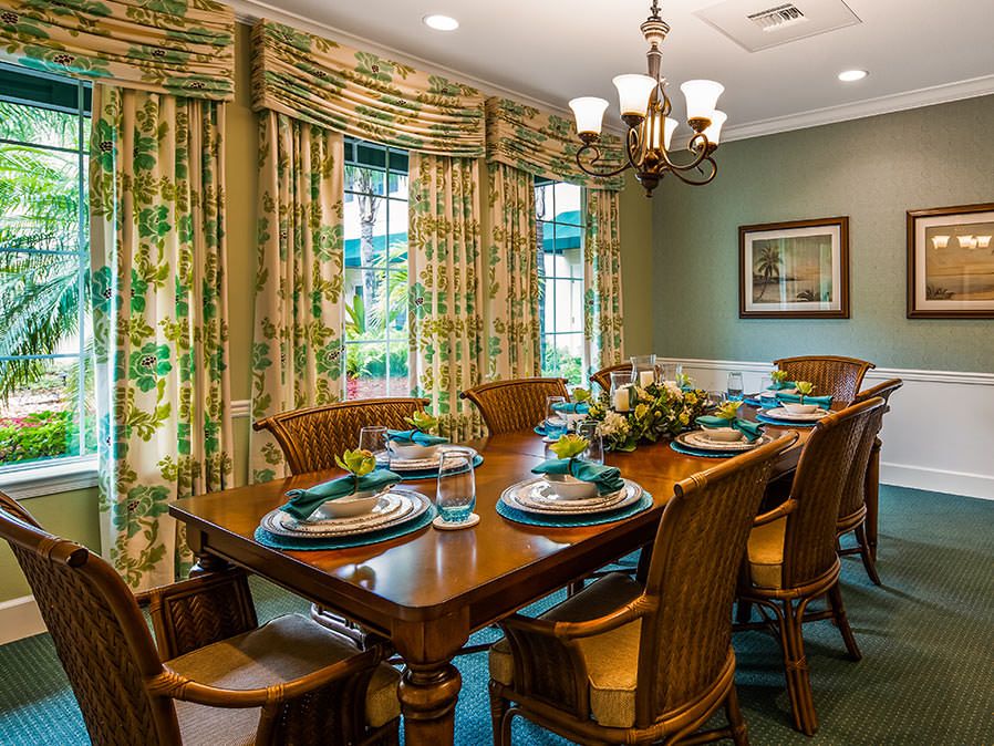A beautifully arranged dining room with a wooden table and chairs, surrounded by elegant curtains and illuminated by a chandelier.