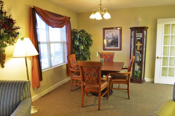 A cozy dining room with a wooden table and chairs, decorated with plants and a glass cabinet.