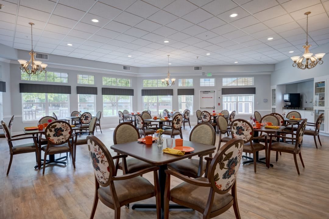A well-lit dining room with multiple tables and chairs, featuring large windows and elegant decor.