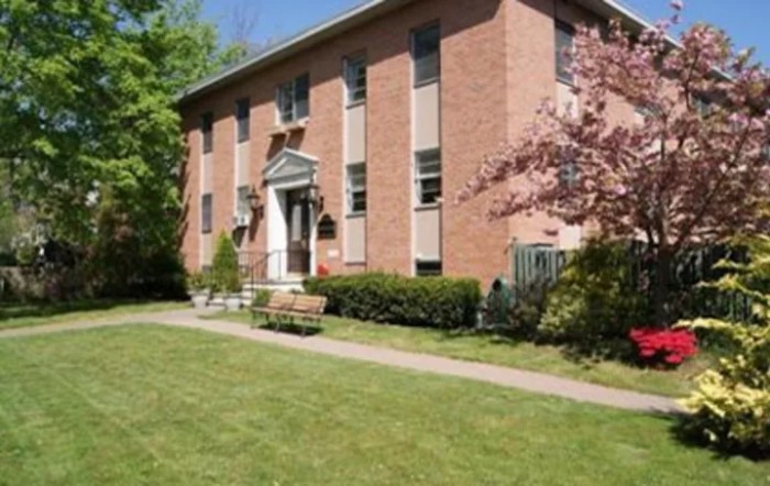 A brick residential building with a neatly trimmed lawn and trees, showcasing a spring setting.