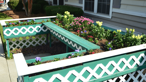 A beautifully arranged raised garden bed with colorful flowers and a decorative green and white fence.