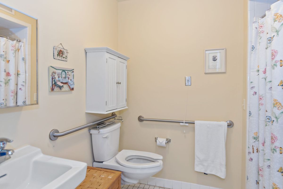 A bathroom equipped with accessibility features includes grab bars, a toilet, a towel, and wall-mounted storage.