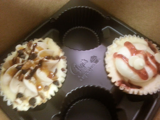 A delightful pair of mini cupcakes, one topped with chocolate and nuts, the other with a swirl of creamy frosting and a berry drizzle.