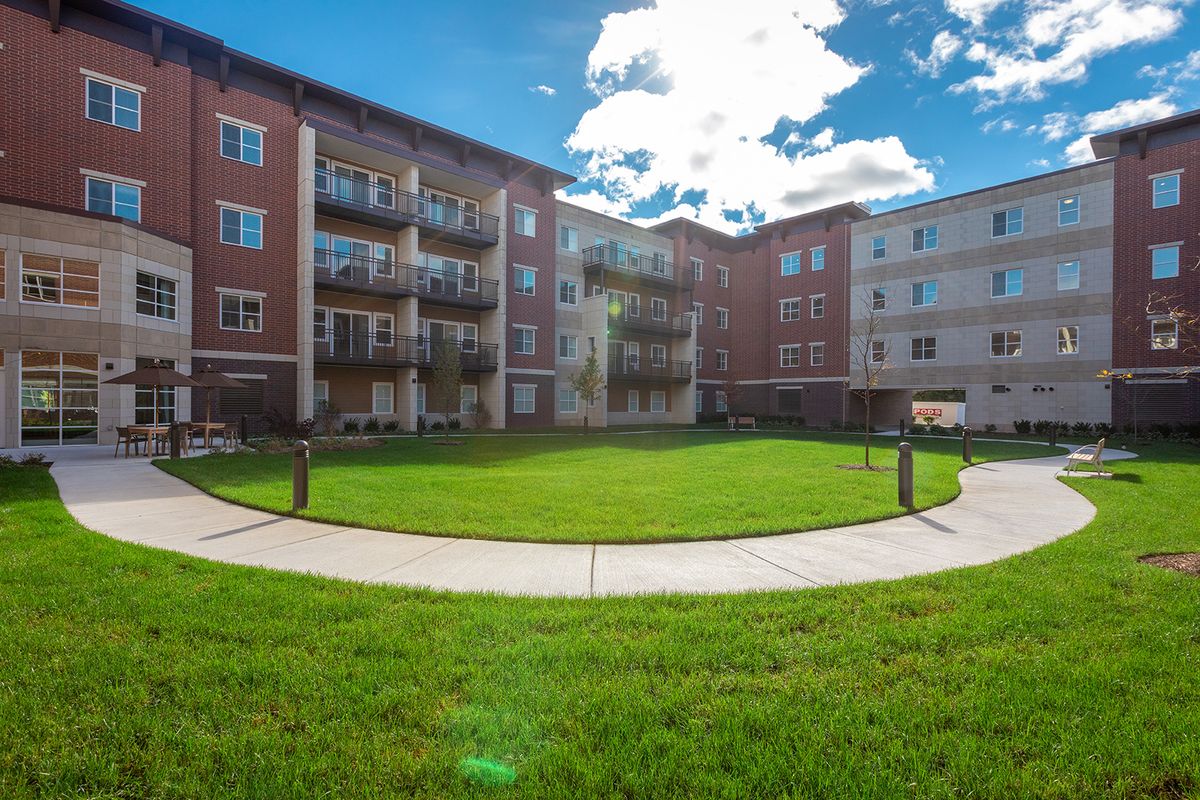 A residential apartment complex with a green courtyard and balconies under a partly cloudy sky.