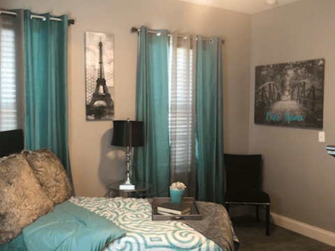 A stylish bedroom featuring teal curtains, an Eiffel Tower artwork, and coordinated bedspread.