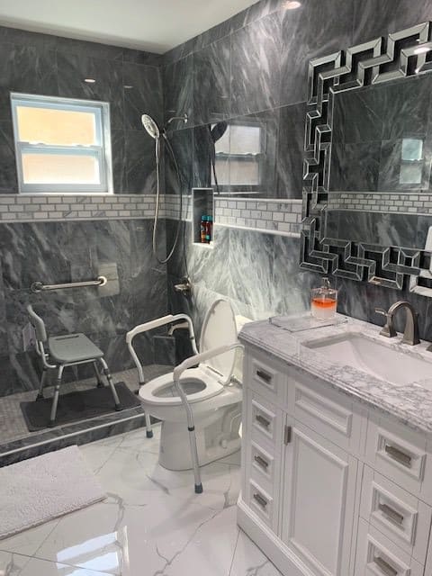 A modern, accessible bathroom featuring marble tiles, a walk-in shower with grab bars, and a toilet equipped with safety rails.