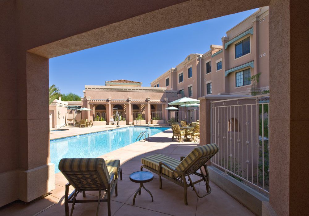 Outdoor hotel swimming pool area with lounge chairs and a fenced patio.
