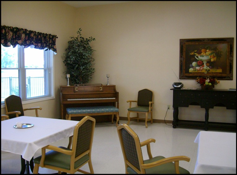 A cozy room with a piano, chairs, and tables, featuring a window and decorative elements.