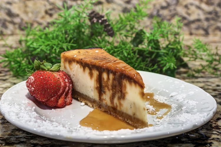 A slice of cheesecake drizzled with caramel sauce, served with fresh strawberries.