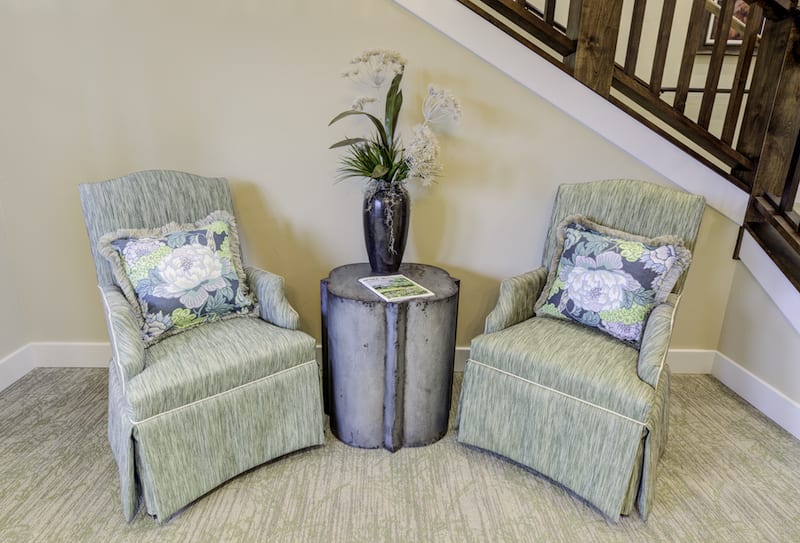 A cozy seating area featuring two armchairs with floral pillows, a central round table, and a decorative vase with plants.