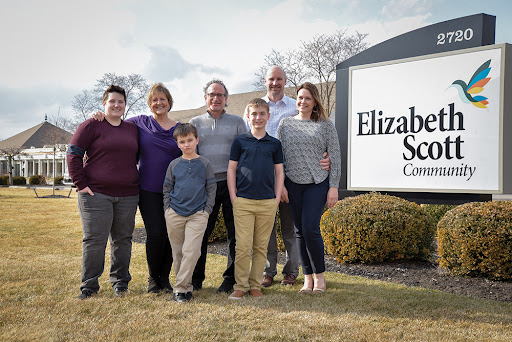 A cheerful family poses together outside the Elizabeth School, showcasing a sense of community and togetherness.