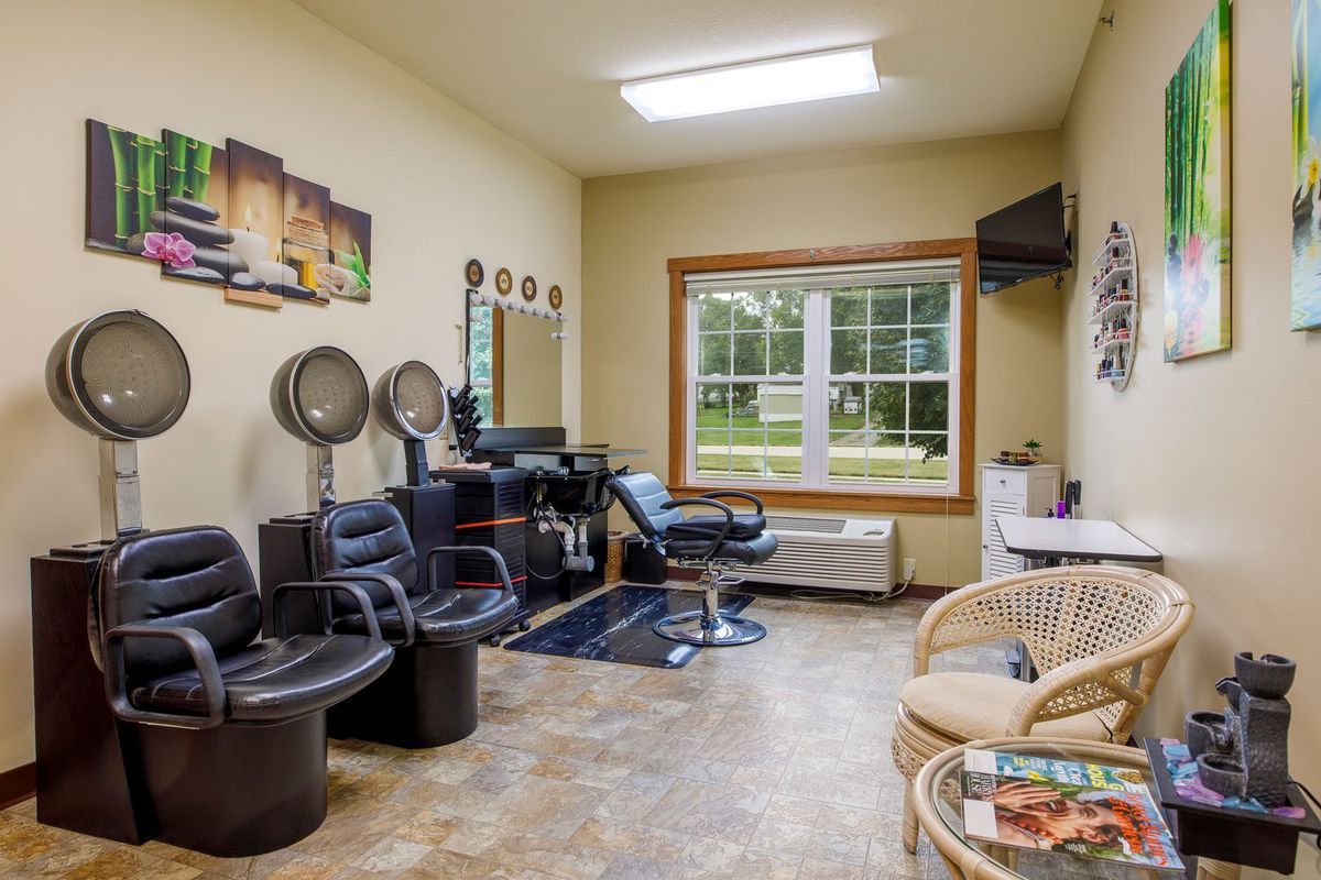 A cozy hair salon with chairs, mirrors, and drying stations, illuminated by natural light from a large window.