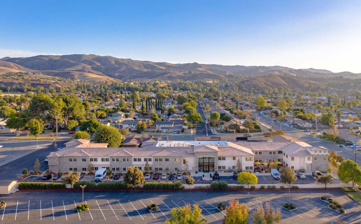 Aerial view of a building with a parking lot, surrounded by a residential area and mountains in the background.