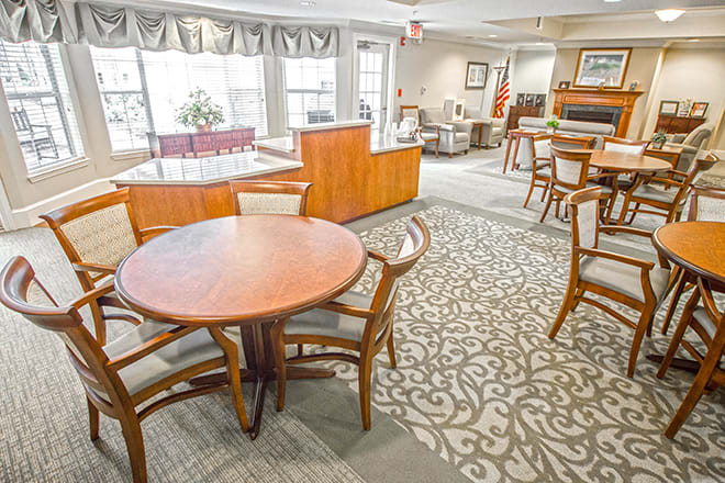 A spacious and bright dining area with wooden tables and chairs, featuring large windows and patterned carpet.