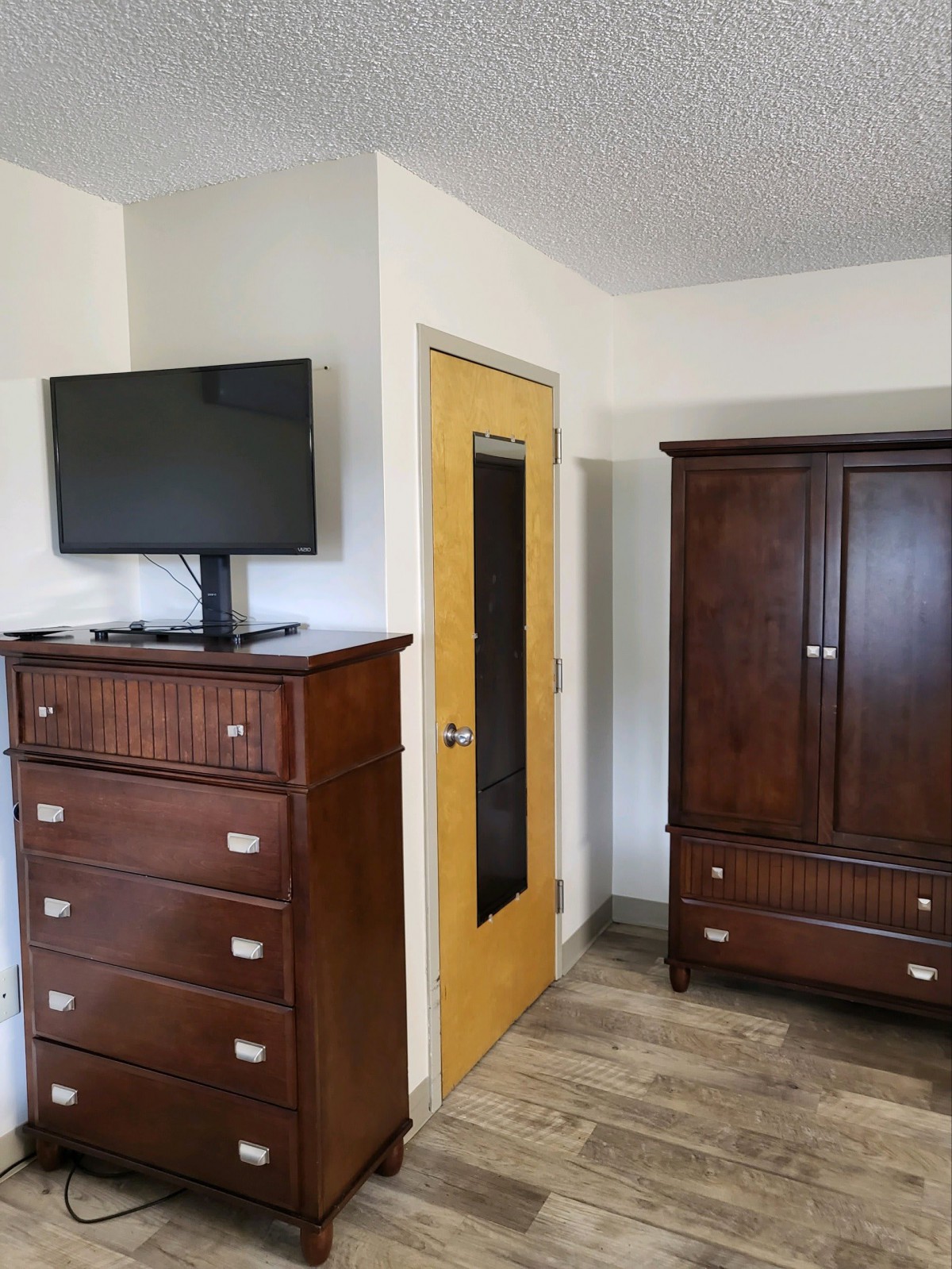 A room featuring a dresser with a television on top, a wardrobe, and a wooden door.