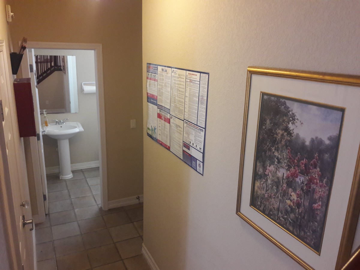 A hallway with a view into a bathroom, displaying a sink, calendar, and framed painting.