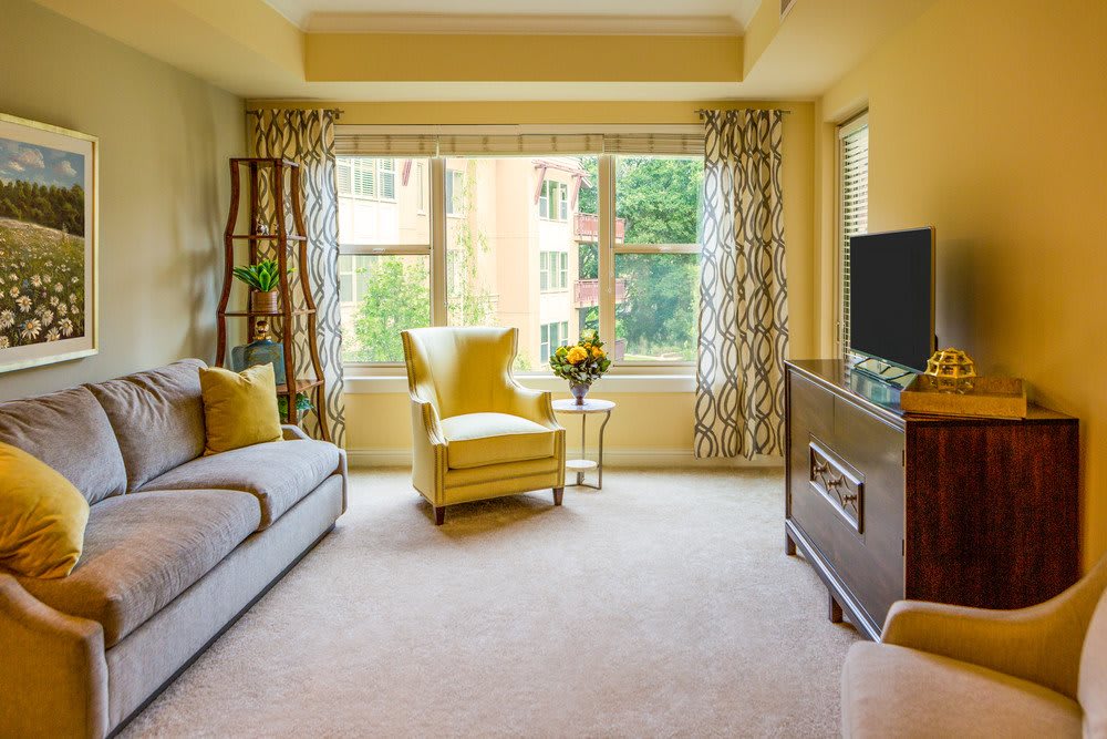 A cozy living room with a modern design, featuring a yellow armchair, sofa, and large window with patterned curtains.