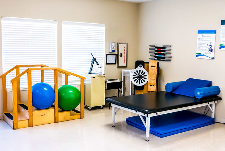 A well-equipped physical therapy room with exercise balls and a treatment table.