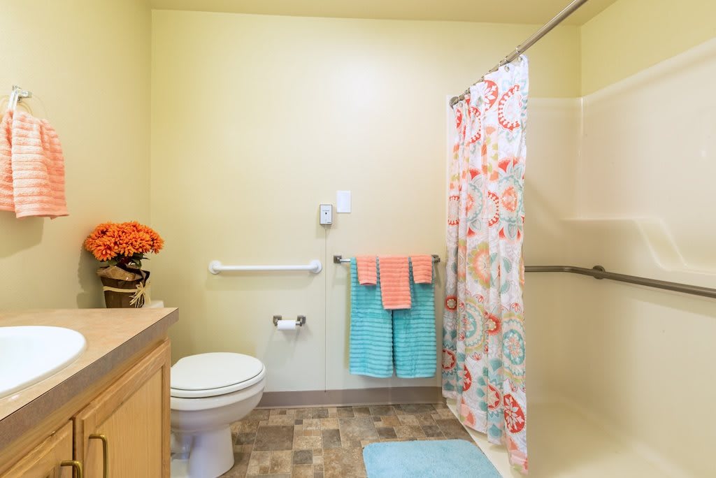 A clean and brightly decorated bathroom with a floral shower curtain and colorful towels.