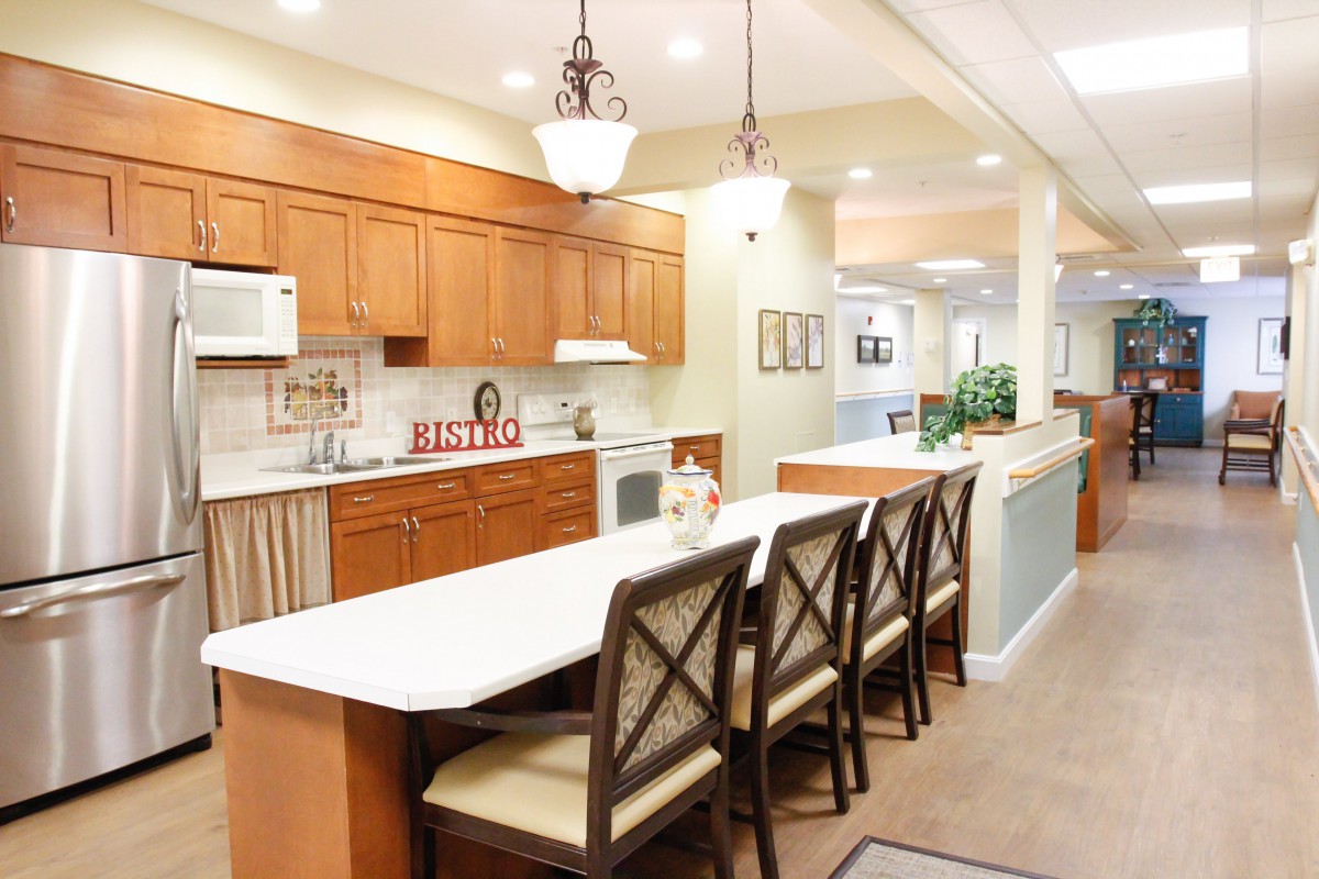 A modern kitchen interior featuring a long countertop with chairs, wooden cabinets, and elegant lighting.
