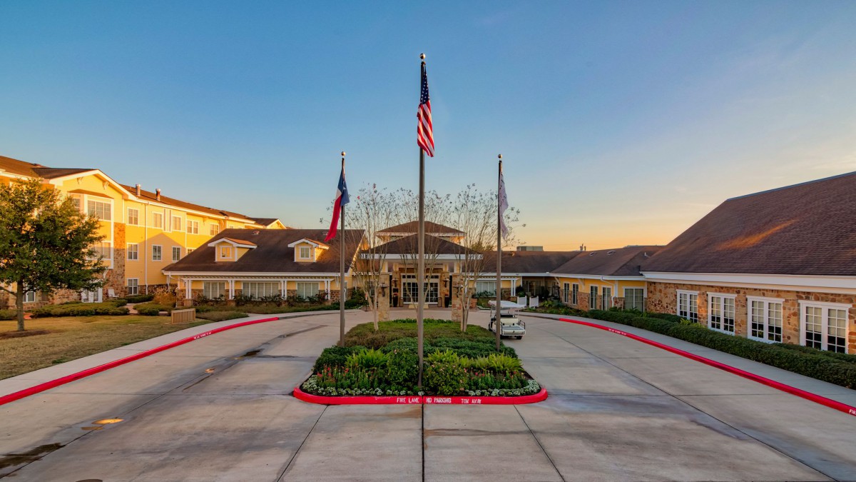 A building entrance with flags and a landscaped driveway at sunset.
