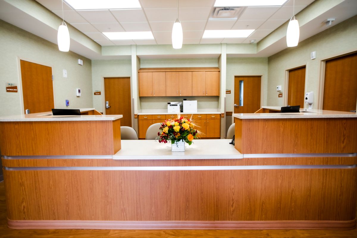 A well-lit reception area with a wooden desk and floral arrangement.