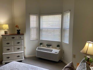 A cozy bedroom corner featuring a bay window with closed blinds, a dresser with an ornament, and an air conditioning unit beneath the window.