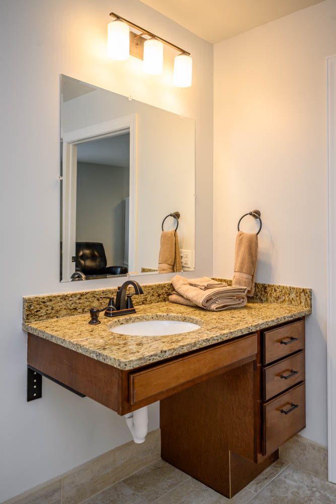 A bathroom with a granite countertop and a sink, featuring neatly folded towels and a mirror above.