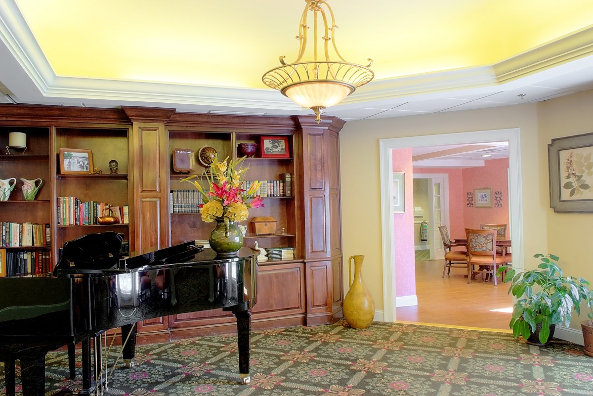 A cozy lounge area featuring a grand piano, bookshelves, and elegant decor.