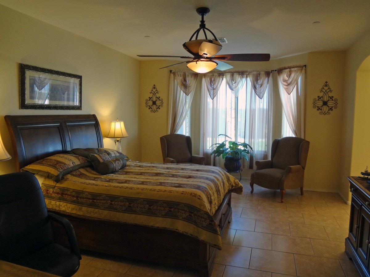 A cozy bedroom with a large bed, two chairs by the window, and a ceiling fan.