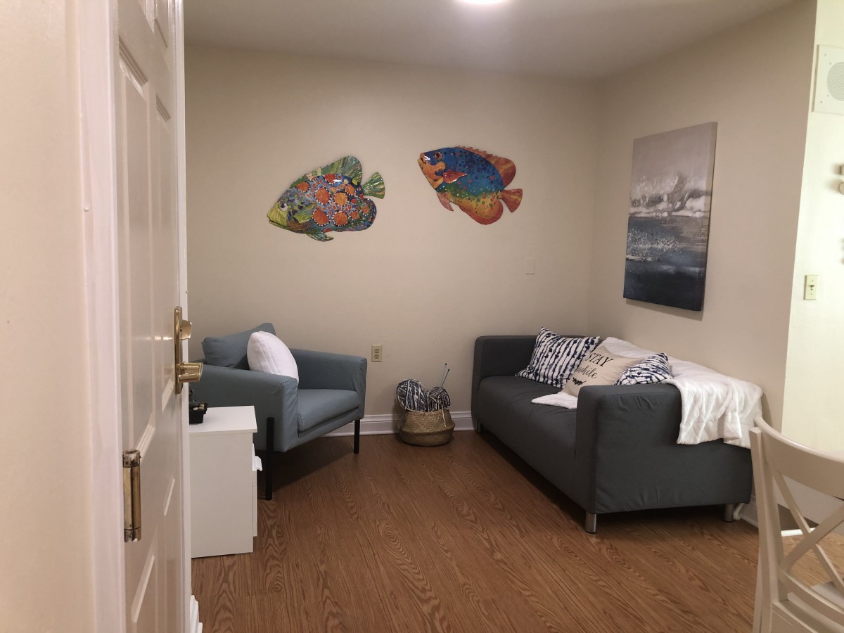 A cozy living room with a sofa and armchair, featuring wall art and wooden flooring.