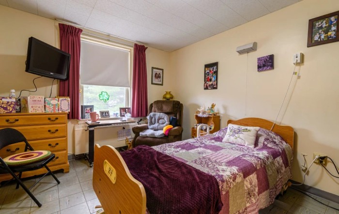 A cozy bedroom with a single bed, armchair, and desk near the window.