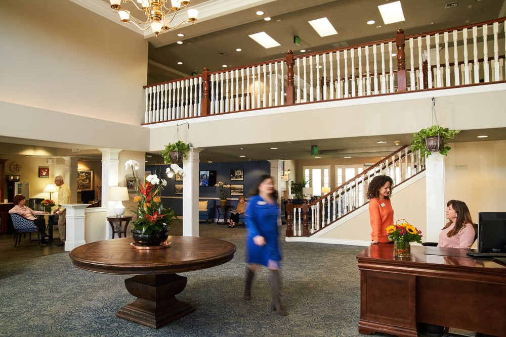 A spacious lobby with a central table, decorative flowers, and people walking through the reception area.