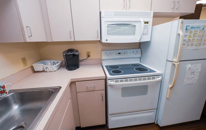 A compact kitchen corner featuring a stove with an overhead microwave and a coffee maker on the countertop.
