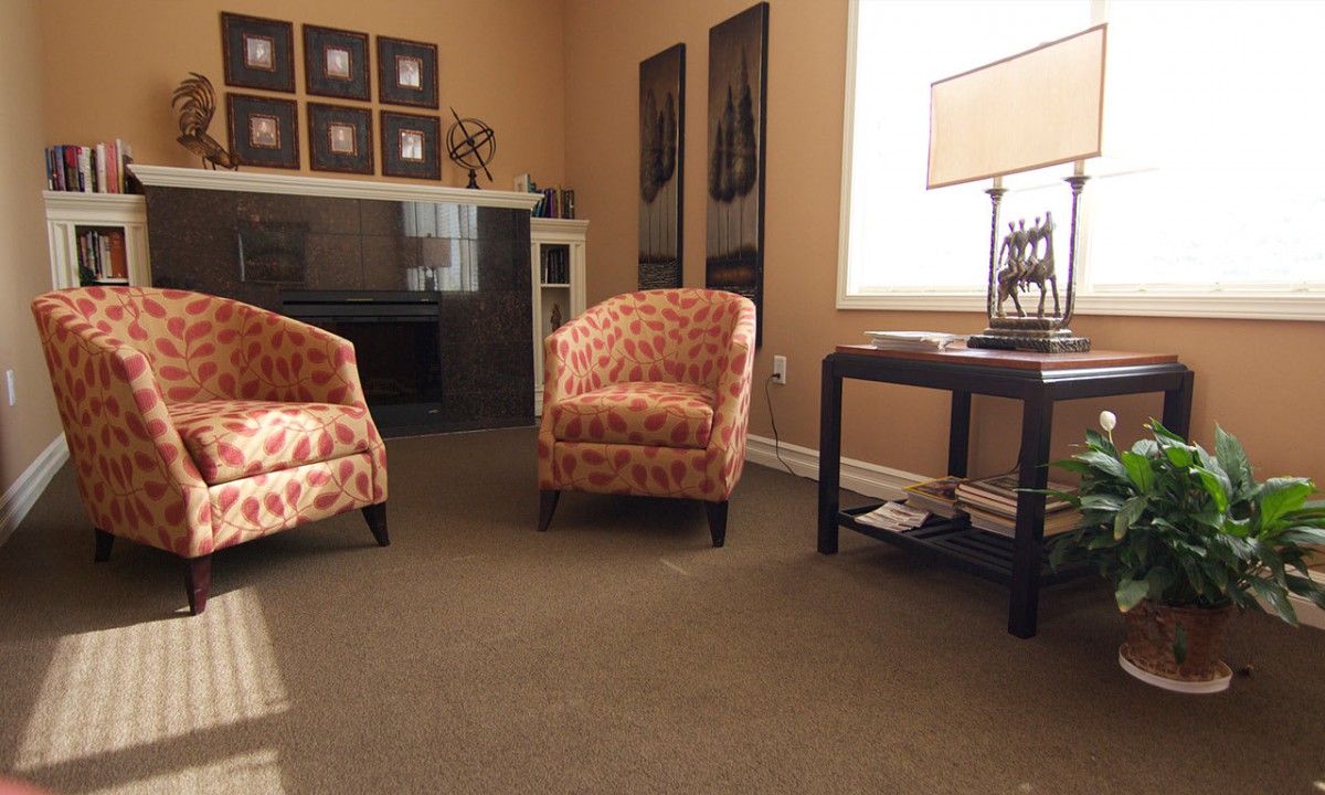 A cozy living room featuring two patterned chairs, a side table with a lamp, and wall art.