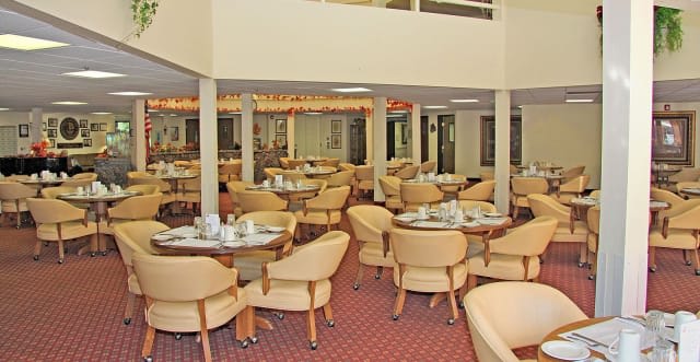 An empty restaurant dining area with neatly arranged tables and chairs on a carpeted floor.