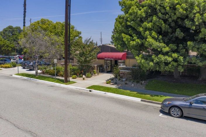 A street view with a building having a red awning, surrounded by trees and a passing car.