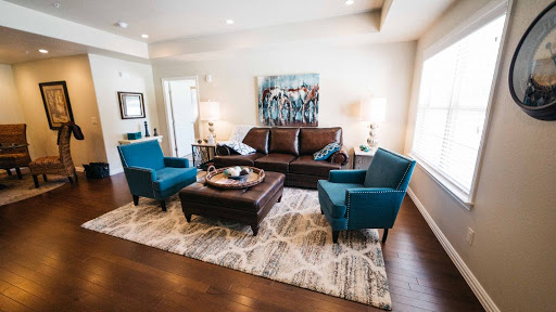 A stylish modern living room featuring a brown sofa and teal accent chairs, centered around a coffee table on a patterned area rug.