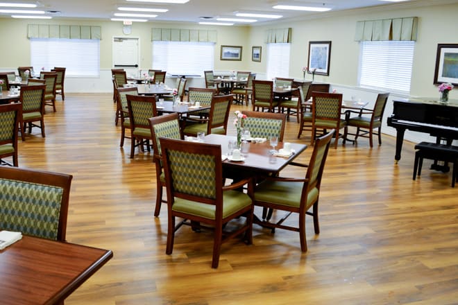 An empty dining room with neatly arranged tables and chairs on a wooden floor.
