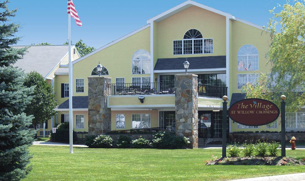A sunny day view of a multistory residential building with a yellow exterior, stone details, and an American flag in front.