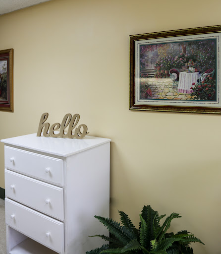 A cozy interior featuring a white chest of drawers with decorative paintings on the wall and a welcoming 'hello' sign.
