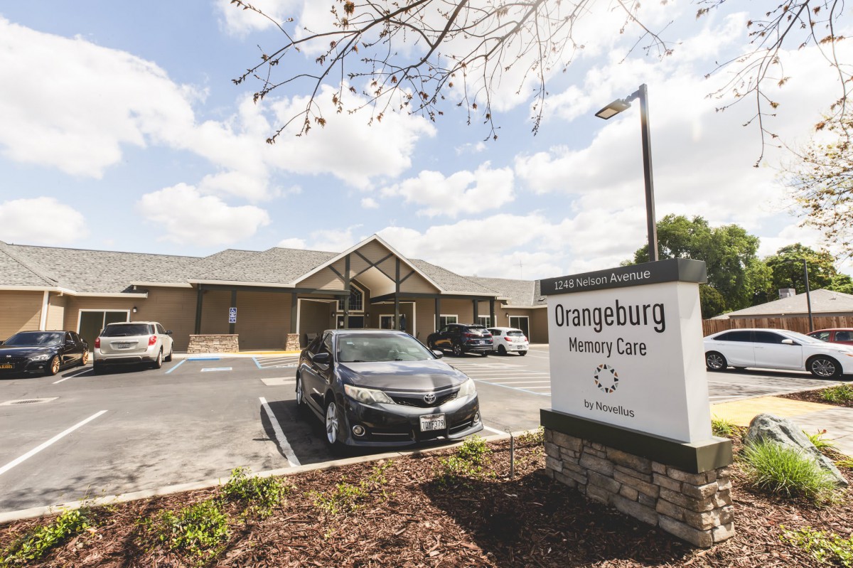 A nursing home with a parking lot and sign under a cloudy sky.