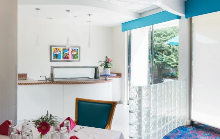 A modern and bright restaurant interior with colorful artwork, stylish furnishings, and a large window overlooking greenery.