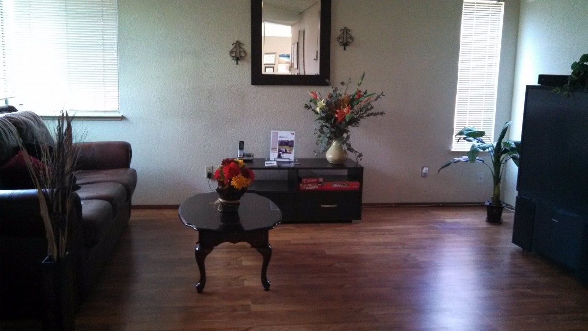 A cozy living room with a central table, decorative flowers, and a wall-mounted mirror.