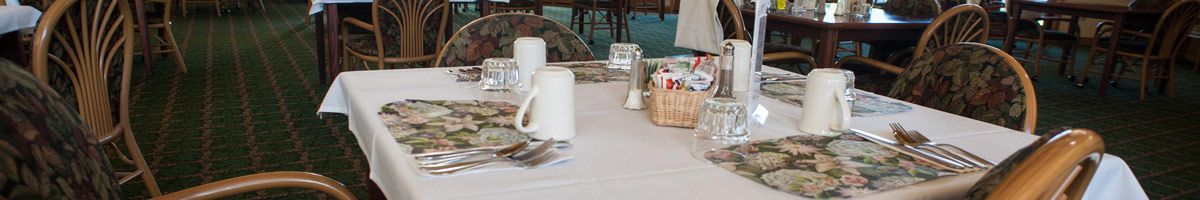 A dining table set with mugs, condiments, and a basket of items in a restaurant setting.