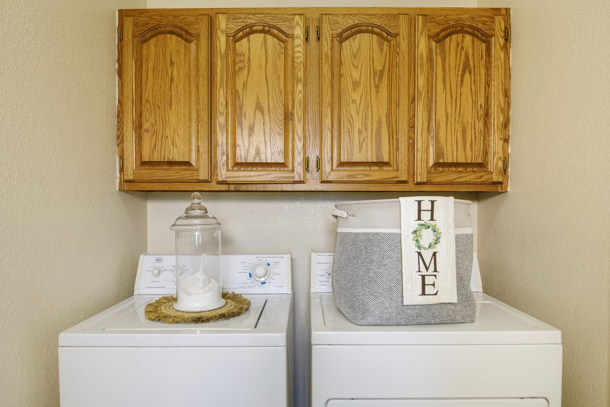 A cozy laundry room with wooden cabinets, a washing machine and dryer, featuring a decorative storage basket.