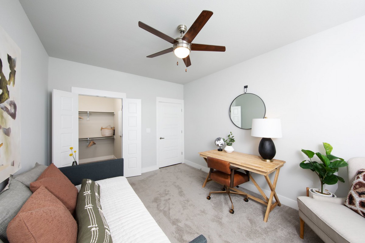 A modern bedroom with a desk, chair, and ceiling fan.